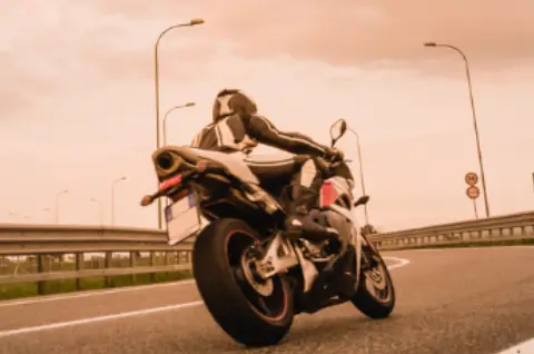 A motorcyclist in a black and white suit rides a sport bike on a highway under a cloudy, orange-tinted sky